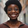 Close up cheerful African woman in glasses sincerely smiling at camera outdoors. Carefree dark-skinned girl looking happy standing on the street